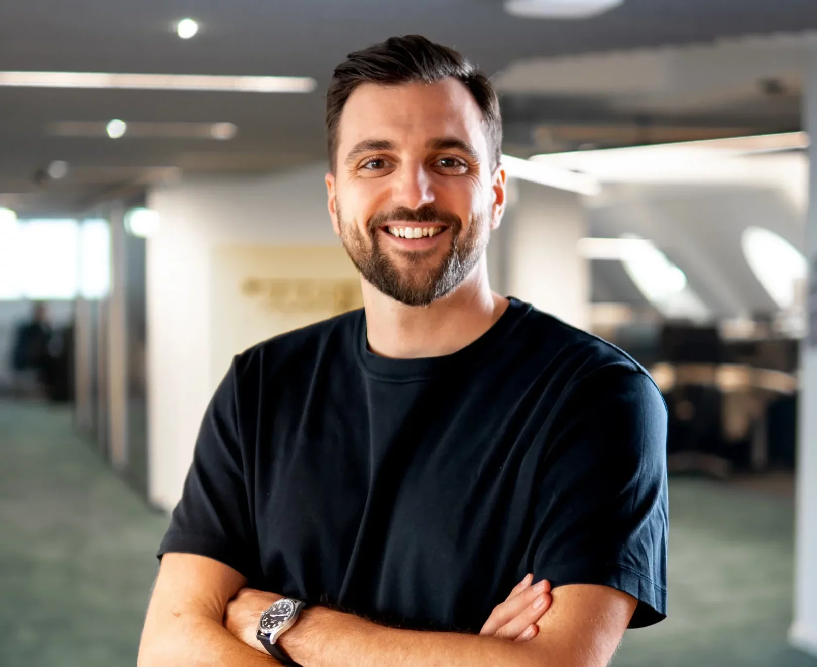 Foto von Mathias Burger, seines Zeichens Head of B2B Customer Education bei kununu, der in einem schwarzen T-Shirt in einem Büro in die Kamera grinst.