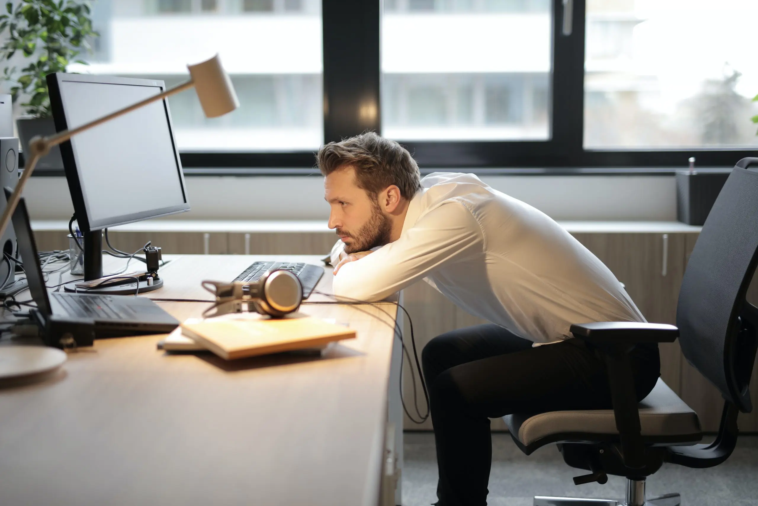 Ein Mitarbeiter sitzt weniger motiviert am Schreibtisch und legt den Kopf auf dem Tisch ab.