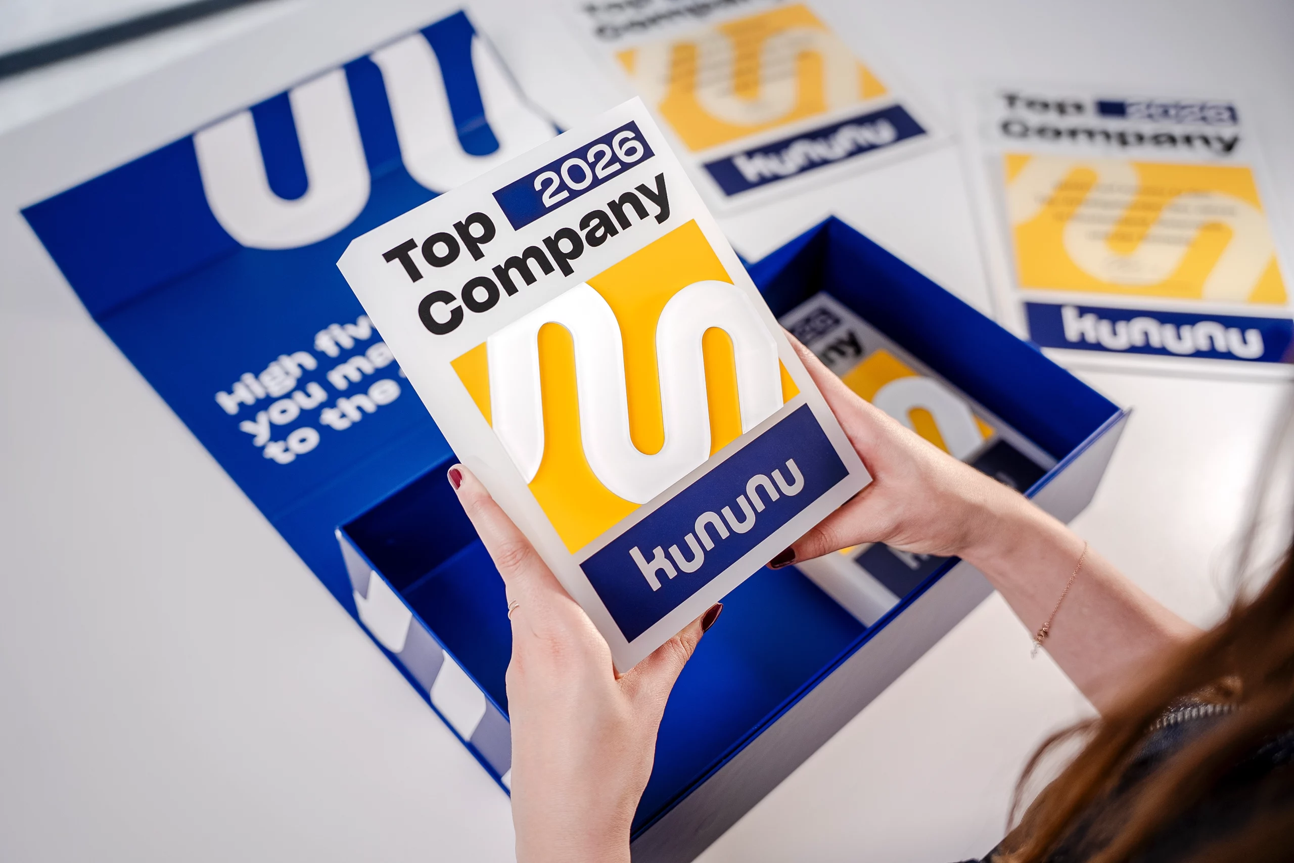 Abgebildet ist die Box, die es beim Kauf der Nutzungslizenz des Top Company Siegels 2026 kostenlos dazu gibt. Jemand hält einen der Awards in beiden Händen.