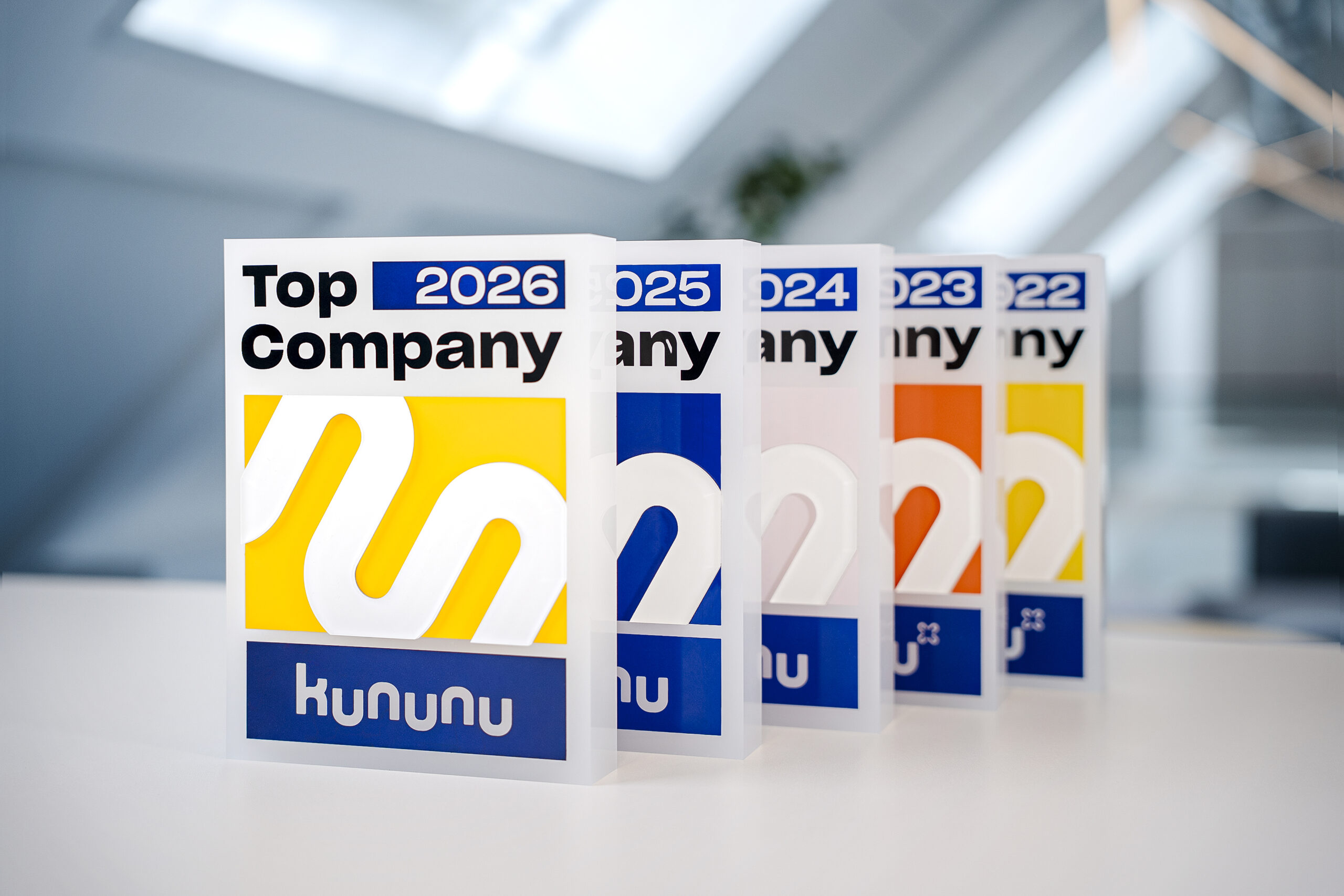 Man sieht die Top Company Awards der letzten 5 Jahren aufgereit auf einem Tisch stehen. Es herrscht eine schöne farbliche Vielfalt durch die unterschiedlichen Award-Farben.
